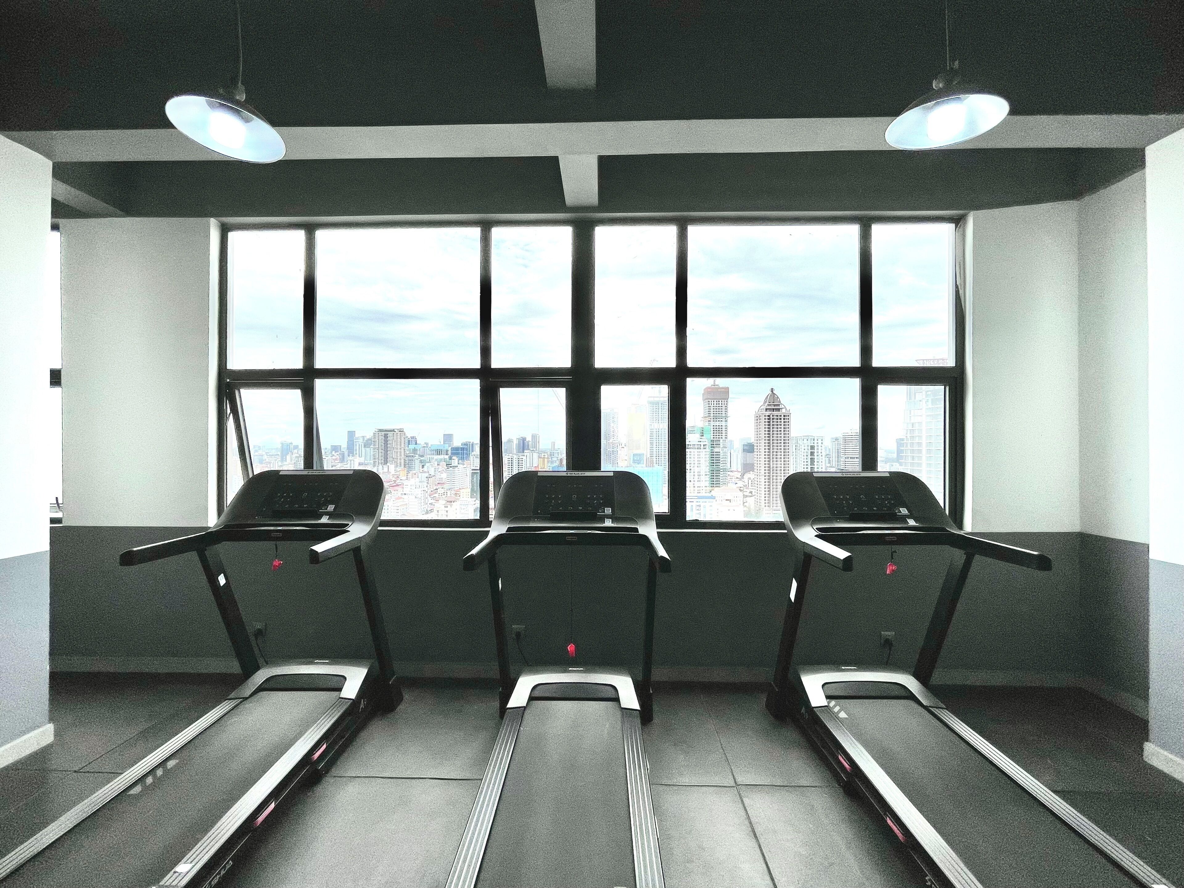 Three treadmills in a room with large windows overlooking a cityscape.