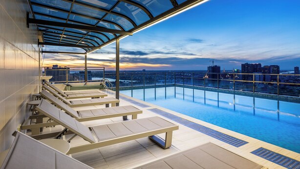 A rooftop infinity pool with lounge chairs and a glass ceiling, overlooking a cityscape at dusk. - SKYCONDO Phnom Penh (Phnom Penh)