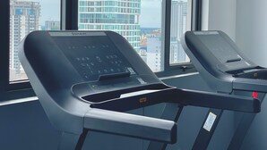 Two exercise machines in a room with large windows overlooking a cityscape. - SKYCONDO Phnom Penh (Phnom Penh)