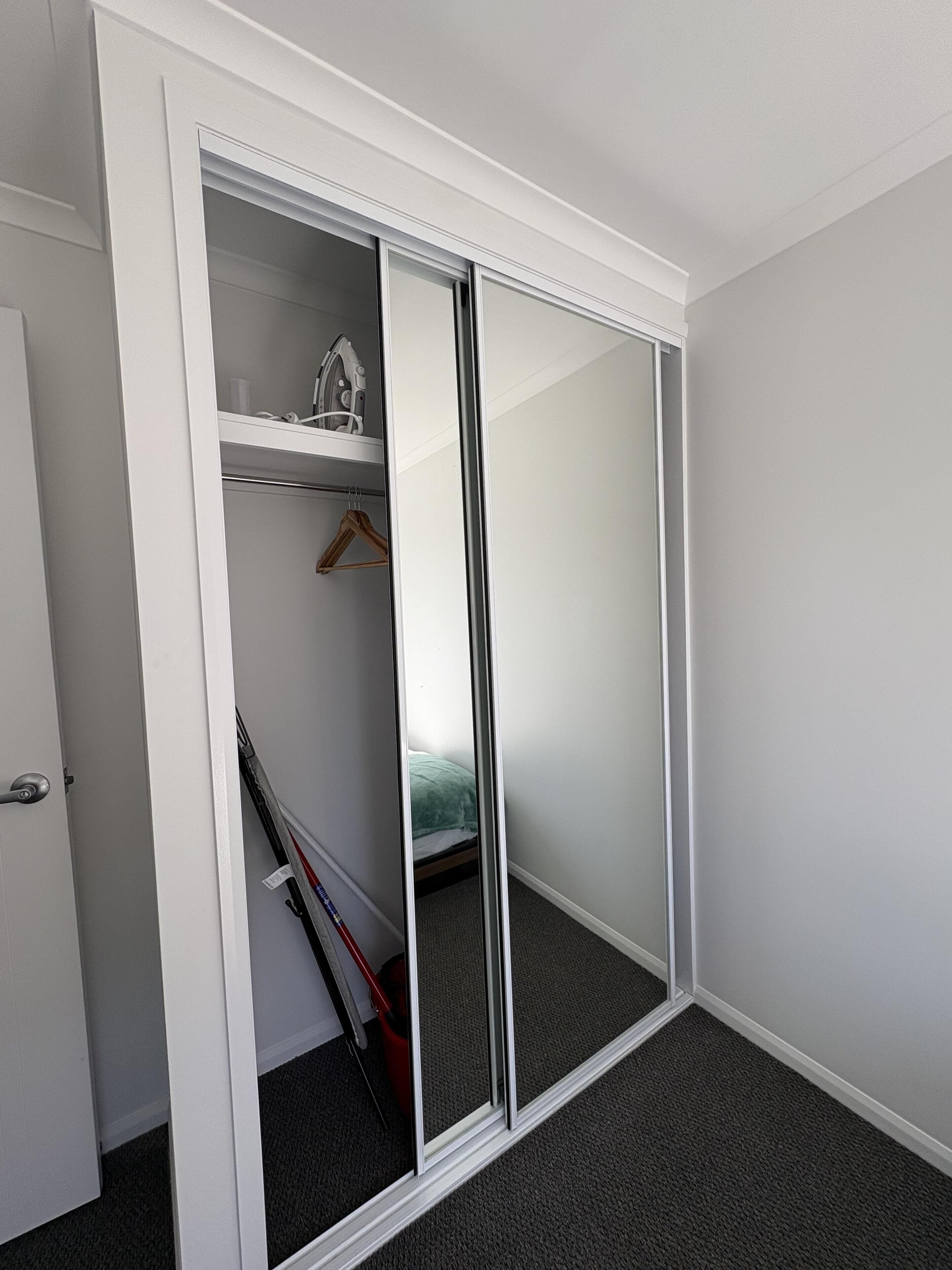 A room with a sliding closet door, a bed, and a small shelf with a hairdryer.