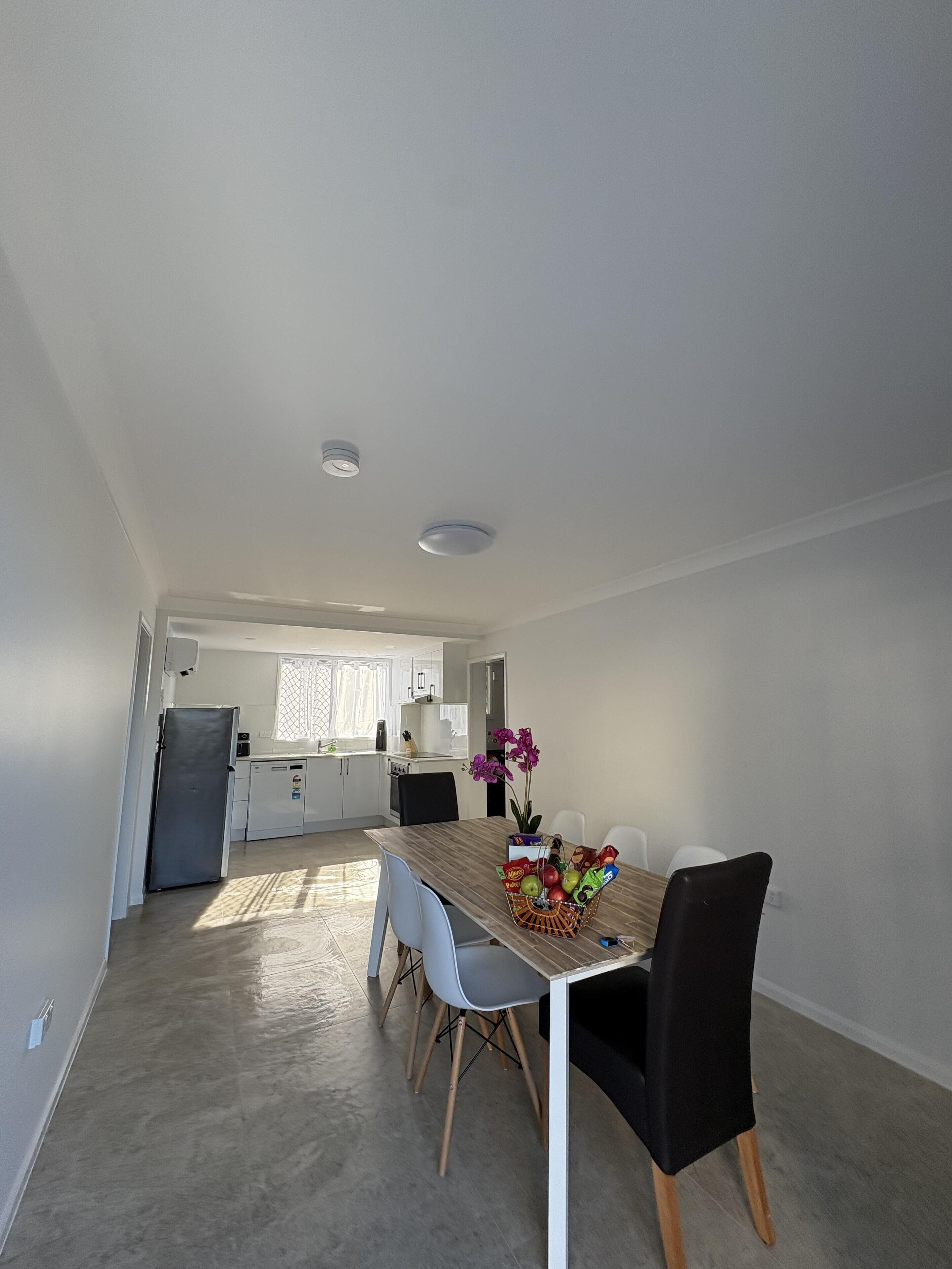 A modern kitchen with white cabinets, a refrigerator, and a dining area with a wooden table and chairs.