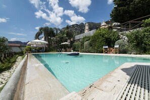 En swimmingpool med klart vand, omgivet af grønt og en stenvæg.