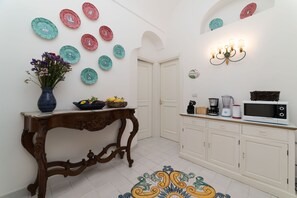 A kitchen with white cabinets, a wooden table with a vase of flowers, and a microwave on the counter. - Art Sea Boutique Villa (Praiano)