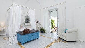 A bedroom with a four-poster bed, a blue chest of drawers, a white sofa, and a balcony with a chair. - Art Sea Boutique Villa (Praiano)
