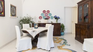 A dining area with a table set for four, surrounded by white chairs. There is a cabinet with glass doors to the right and a wall with framed artwork above the table. - Art Sea Boutique Villa (Praiano)