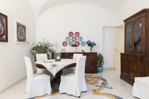 Comedor con una mesa dispuesta para cuatro personas, rodeada de sillas blancas. A la derecha hay un aparador con puertas de cristal y, sobre la mesa, una pared decorada con cuadros.