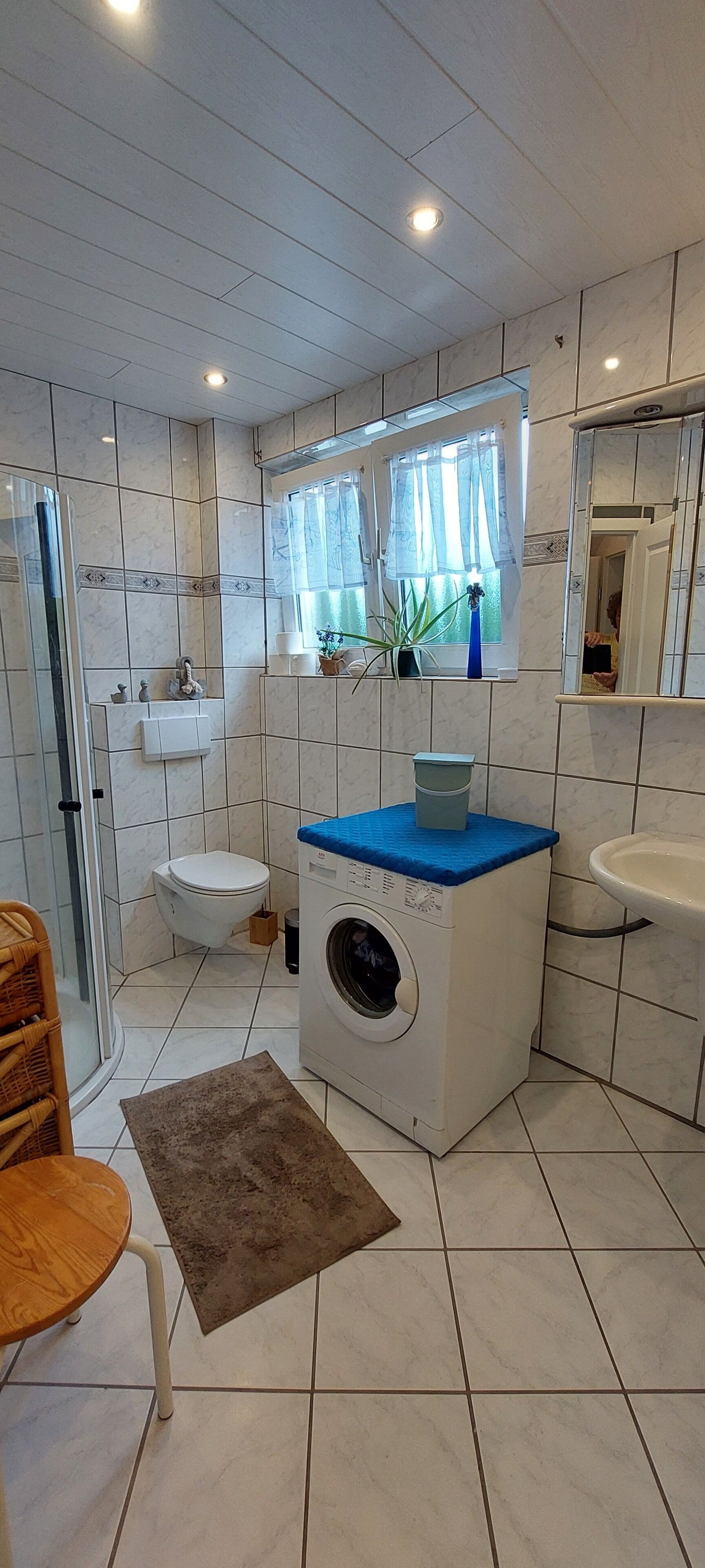 Une salle de bain équipée de toilettes, d’un lave-linge, d’un lavabo et d’une fenêtre avec des rideaux.