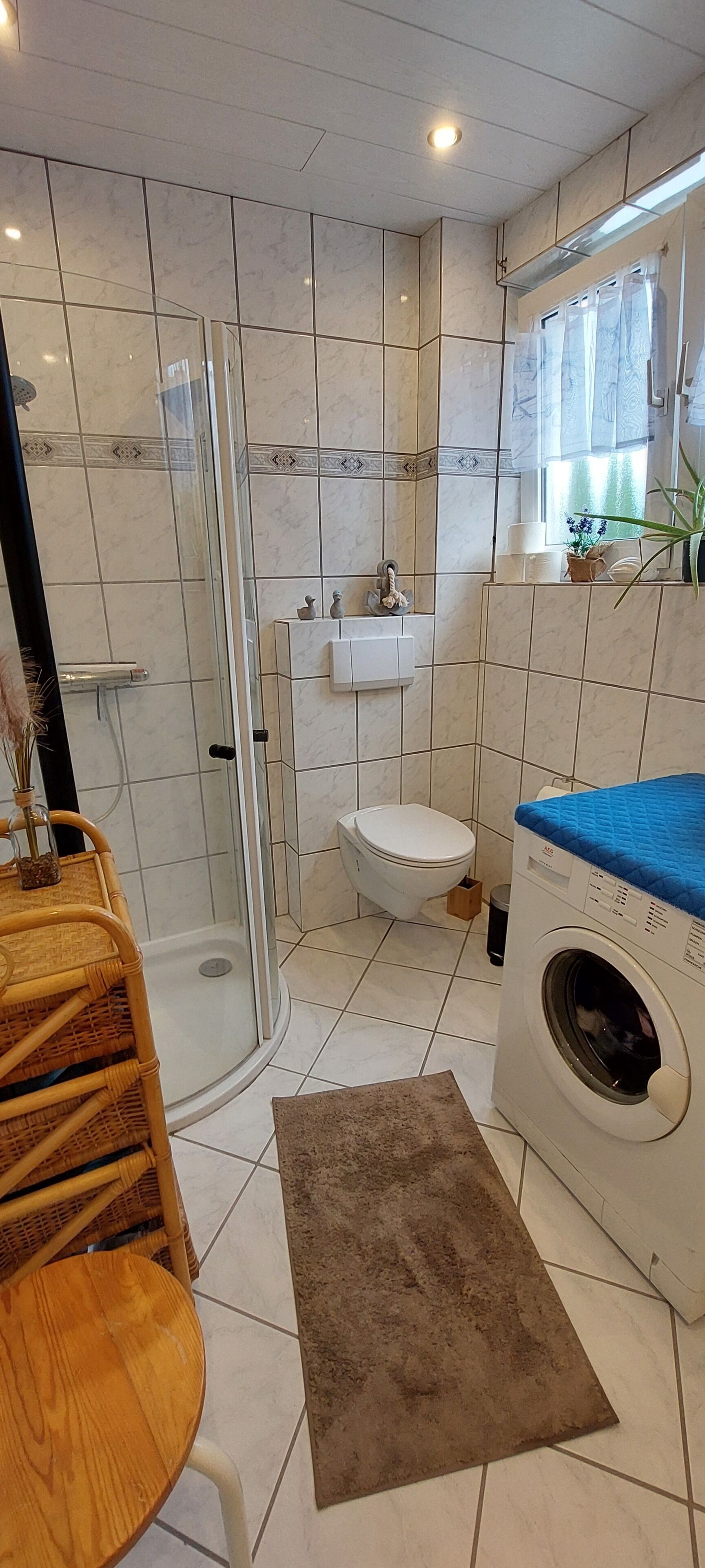 A bathroom with a glass shower enclosure, a toilet, a sink, and a washing machine.