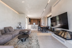 Un salon moderne avec un canapé d’angle, une table basse ronde, un téléviseur à écran plat et une cheminée.