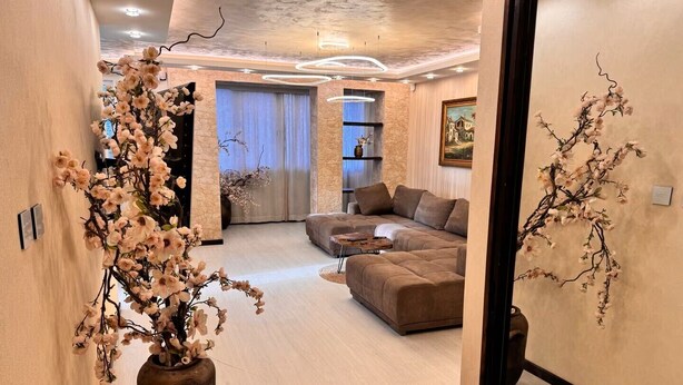 Una sala moderna con un sofá modular, un jarrón grande con flores y una pared de acento de piedra.