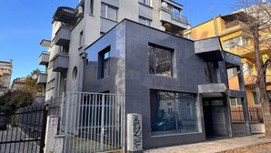 Un edificio moderno de dos pisos con fachada gris, ventanas grandes y entrada protegida por una reja.