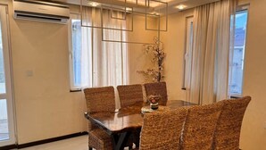 Un comedor con mesa de madera y sillas tejidas, un jarrón con flores y una lámpara moderna.