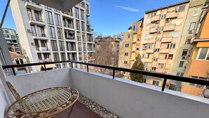 Un balcón con mobiliario de mimbre, vistas a edificios de varios pisos y cielo despejado.