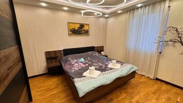 Una camera da letto moderna con pavimento in legno, un letto con biancheria da letto floreale, un quadro appeso al muro e un lampadario dal design originale.