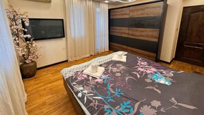 Un dormitorio con cama, televisión, suelo de madera y una lámpara de techo moderna.