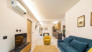 Uma sala de estar moderna com um sofá azul, uma poltrona amarela e uma televisão sobre um móvel de madeira.