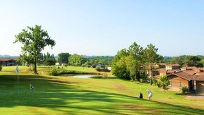 En golfbane med en sø, træer og bygninger i baggrunden.