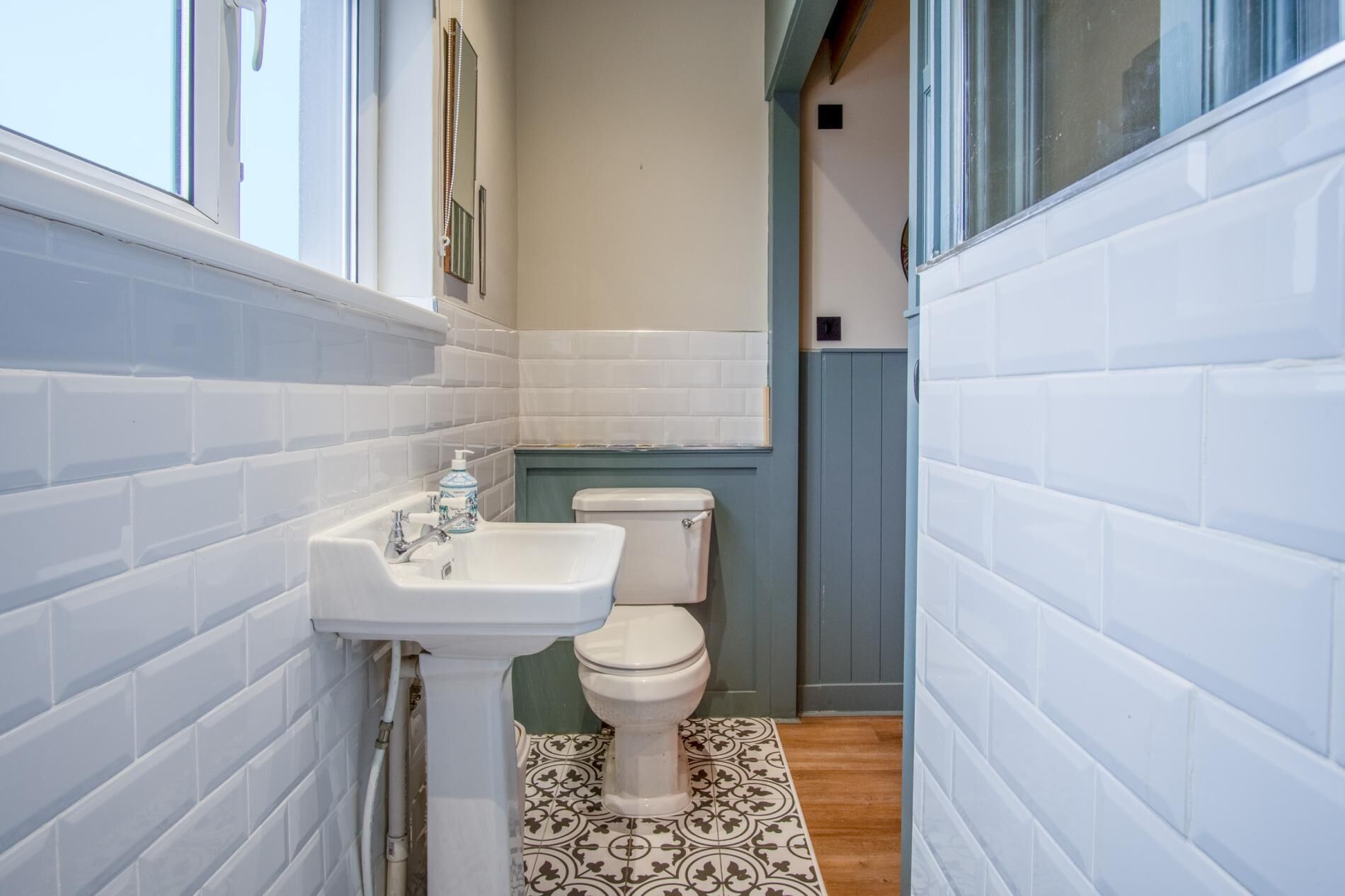 Un bagno stretto con pareti rivestite di piastrelle bianche, un lavandino bianco e un water.