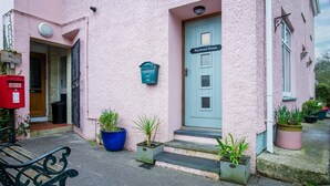 A pink building with a blue door labeled "Raymond House," a mailbox, and potted plants. - Tide & Tee - 2 Bedroom Apartment - Penally - Tenby (Tenby)