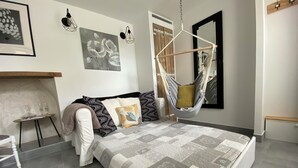 A modern bedroom with a large bed, a hanging chair, and a small table with glasses.