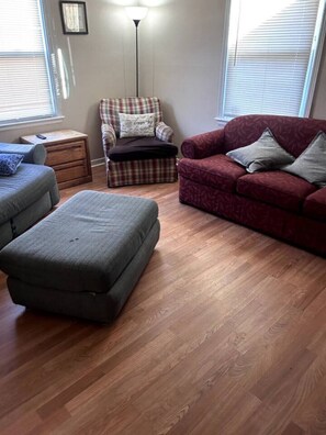 Una sala de estar con un sillón escocés, un sofá rojo y un reposapiés gris.