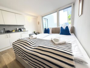 A modern hotel room with a large bed, a view of the outdoors, a kitchenette, and a window with blinds. - Hillside Living Vienna (Vienna)