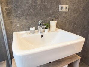 A bathroom sink with a marble countertop, a modern faucet, and a small potted plant. - Hillside Living Vienna (Vienna)
