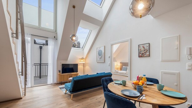 A modern loft-style room with a dining area, a sofa, and a TV. - Hillside Living Vienna (Vienna)