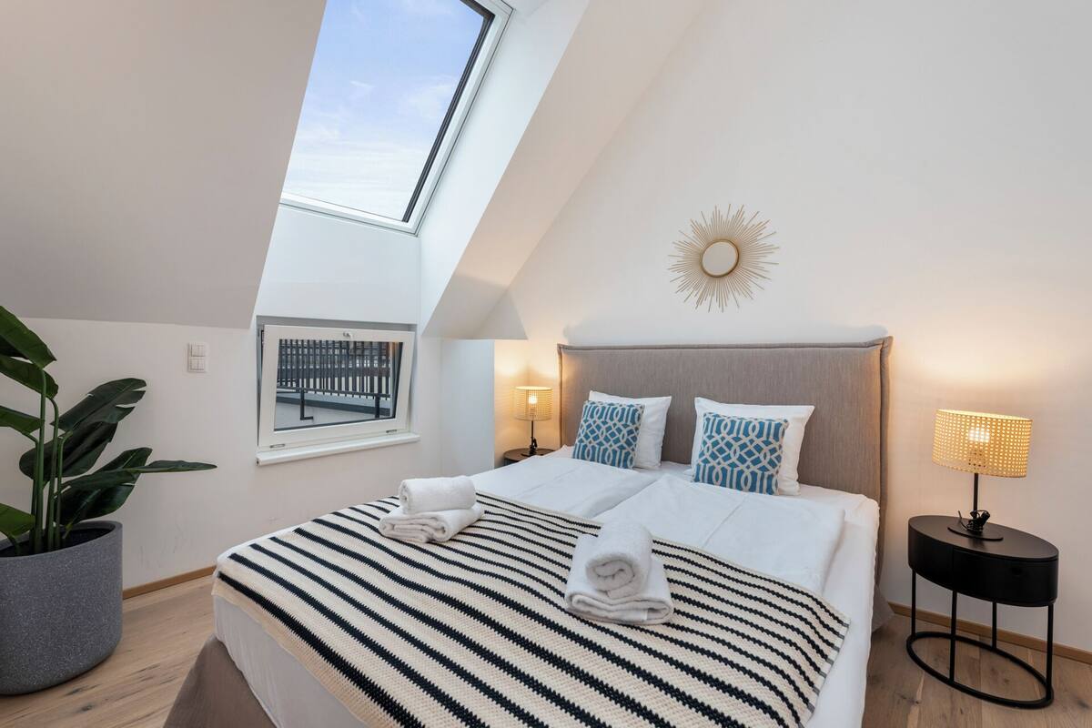 Une chambre avec un puits de lumière, un lit avec une literie à rayures, une décoration murale en forme de soleil et une lampe de chevet.