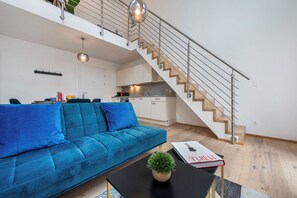 A modern living space with a blue sofa, a staircase, a kitchen, and a dining area. - Hillside Living Vienna (Vienna)