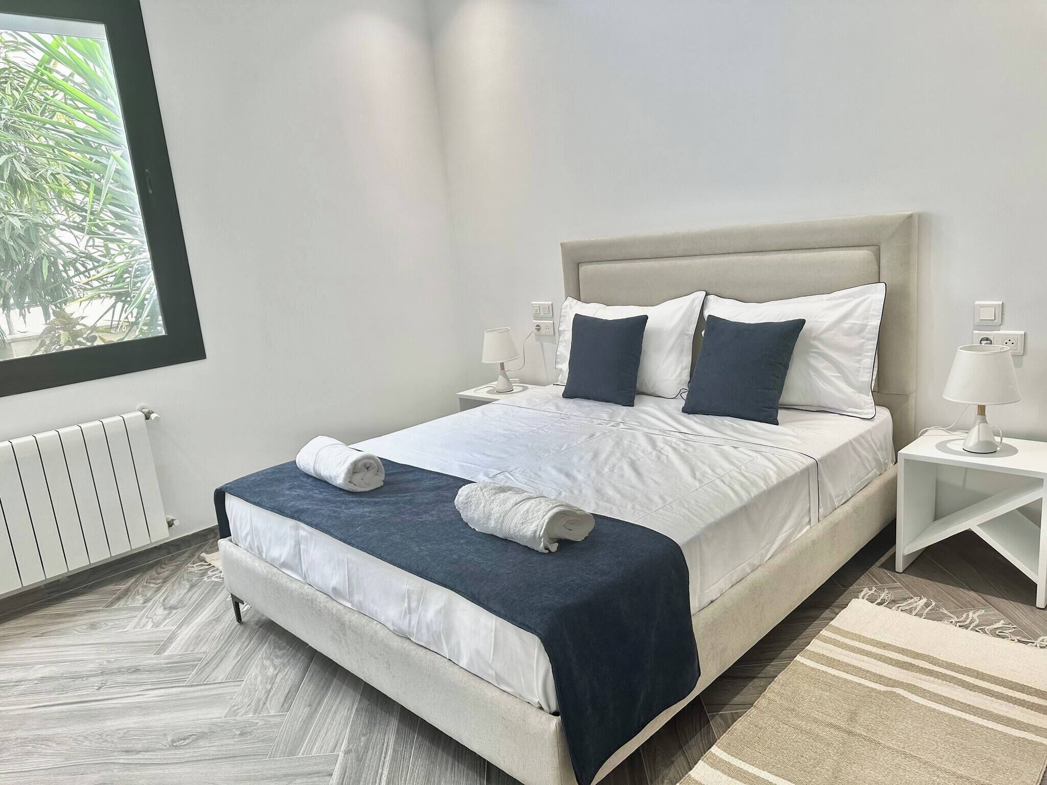 Un dormitorio moderno con una cama, dos mesitas de noche, una ventana y un radiador.
