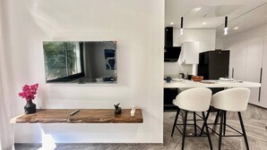 A modern kitchen with white cabinets, a black refrigerator, and a dining area with a wooden table and two white chairs. - Topaz - Bright Apartment Lake 2 (Tunis)