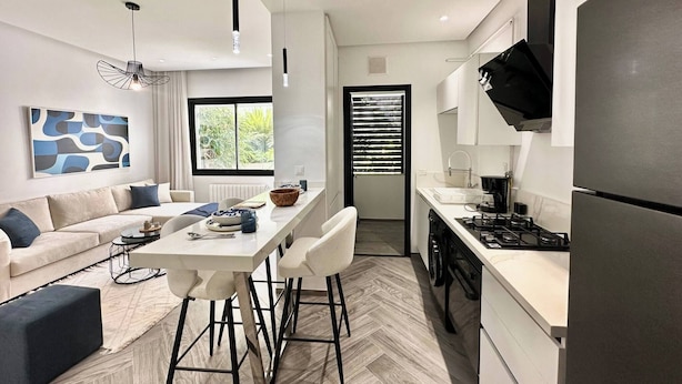 A modern kitchen with a built-in stove, a refrigerator, and a dining area with a white table and chairs. - Topaz - Bright Apartment Lake 2 (Tunis)