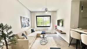 A modern living room with a sofa, coffee table, and a dining area with a chair and a small table. - Topaz - Bright Apartment Lake 2 (Tunis)