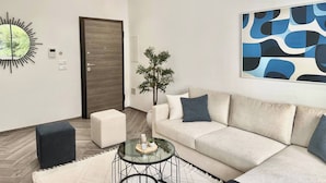 A modern living room with a sofa, a glass coffee table, a decorative mirror, a door, and a wall art piece. - Topaz - Bright Apartment Lake 2 (Tunis)