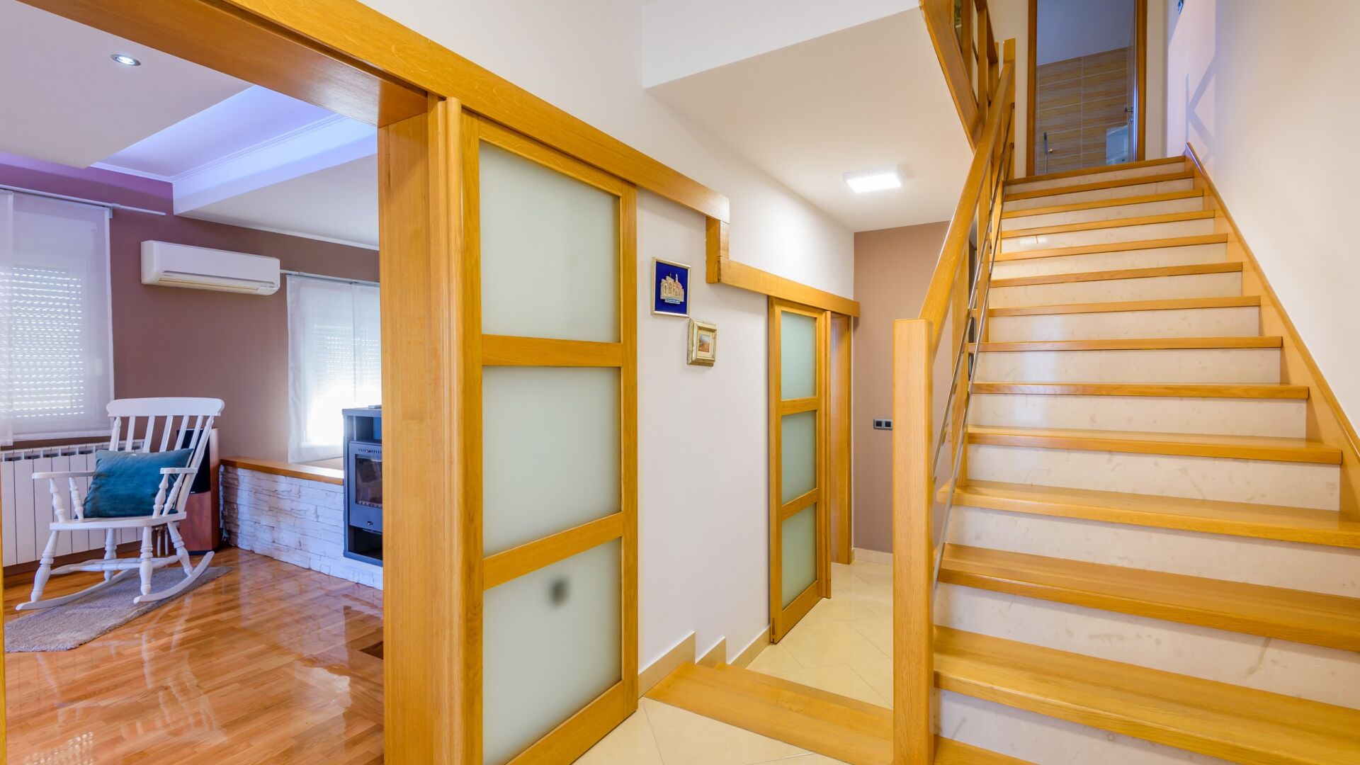 A modern interior with a wooden staircase, a dining area with a rocking chair, and a kitchen with a built-in oven.