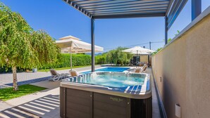 A hot tub area with lounge chairs, a pool, and a covered patio.
