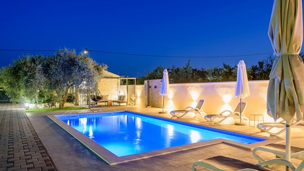A swimming pool with lounge chairs and umbrellas, surrounded by a brick patio and a stone wall.