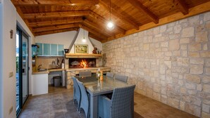 A stone wall kitchen with a stone fireplace, wooden ceiling beams, and a dining area with wicker chairs.