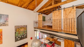 Una habitación tipo loft con entrepiso, vigas de madera, un balcón y obras de arte en las paredes.