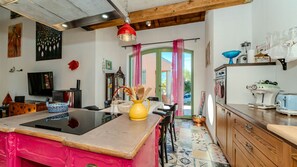 Une cuisine avec un îlot central, un coin repas avec des chaises, un téléviseur et un plafond en bois.