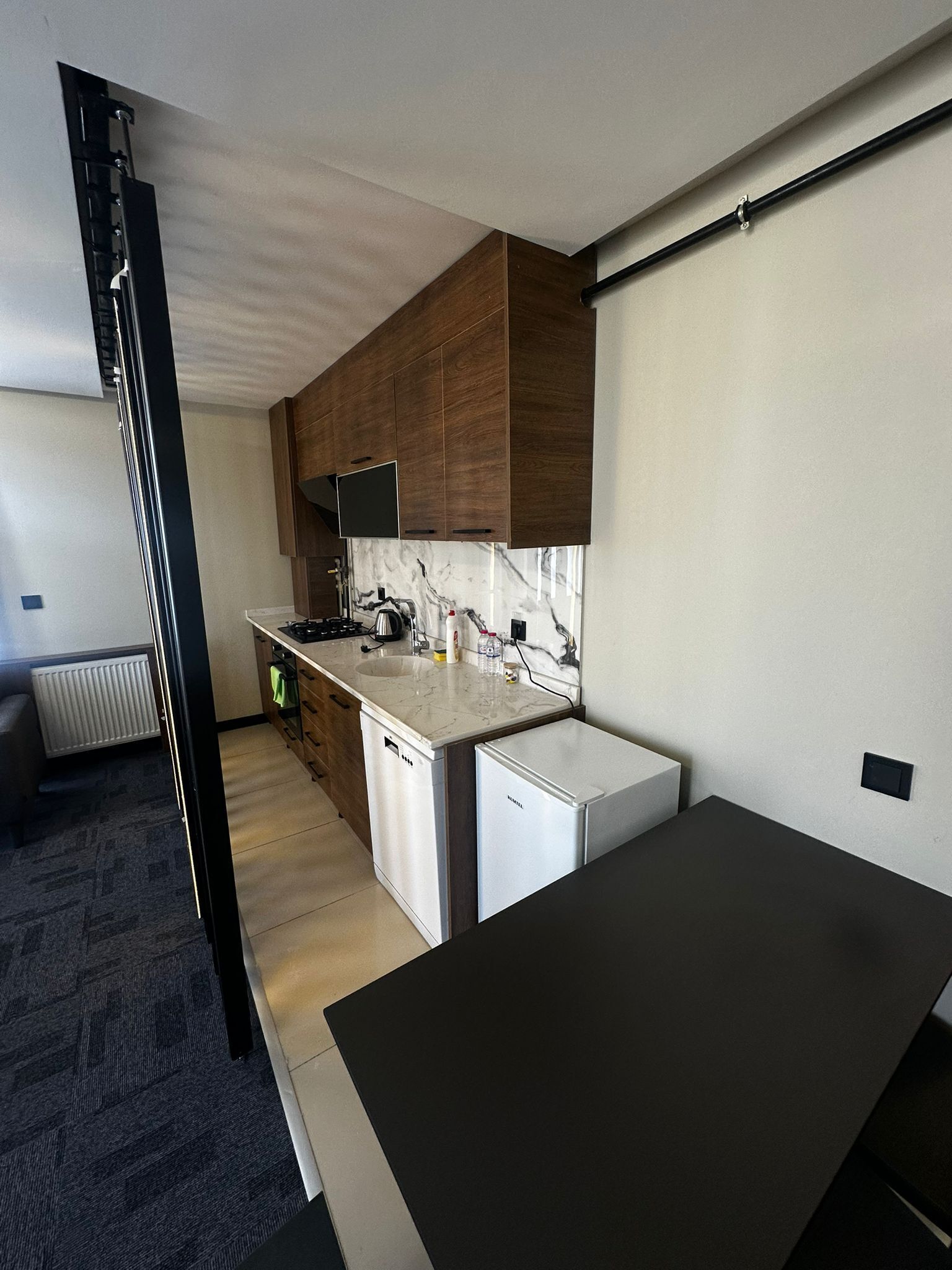 Une cuisine compacte avec des meubles en bois, un plan de travail blanc, un four encastré et un petit réfrigérateur.