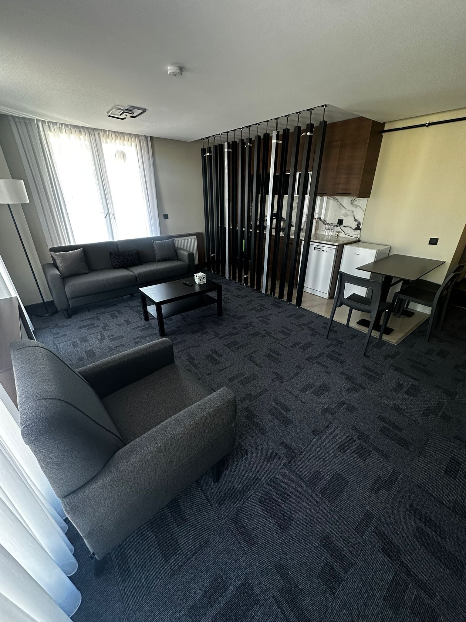 A modern living room with a sofa, coffee table, and a kitchen area with a countertop and appliances.