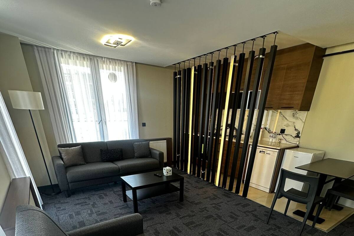 A modern living room with a sofa, a coffee table, a chair, a lamp, and a kitchen area with a refrigerator and stove.