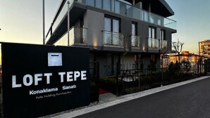 A modern building with a curved facade, balconies, and a sign indicating 'LOFT TEPE' with 'Konaklama' and 'Sani' visible.