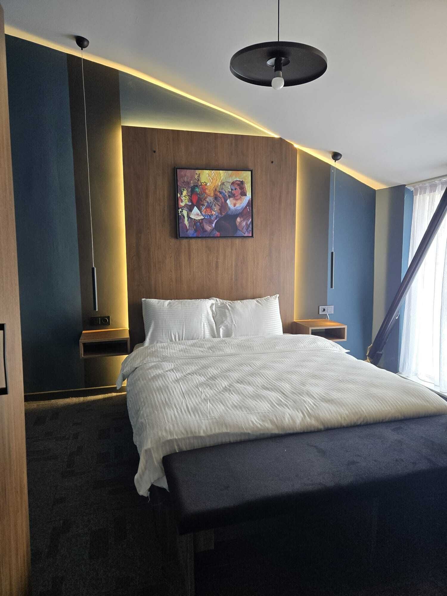 Una habitación de hotel con una cama grande, un cuadro en la pared y una lámpara colgante moderna.