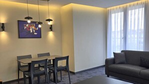 A modern living room with a sofa, a coffee table, a dining table with chairs, pendant lights, and a ceiling-mounted light fixture.