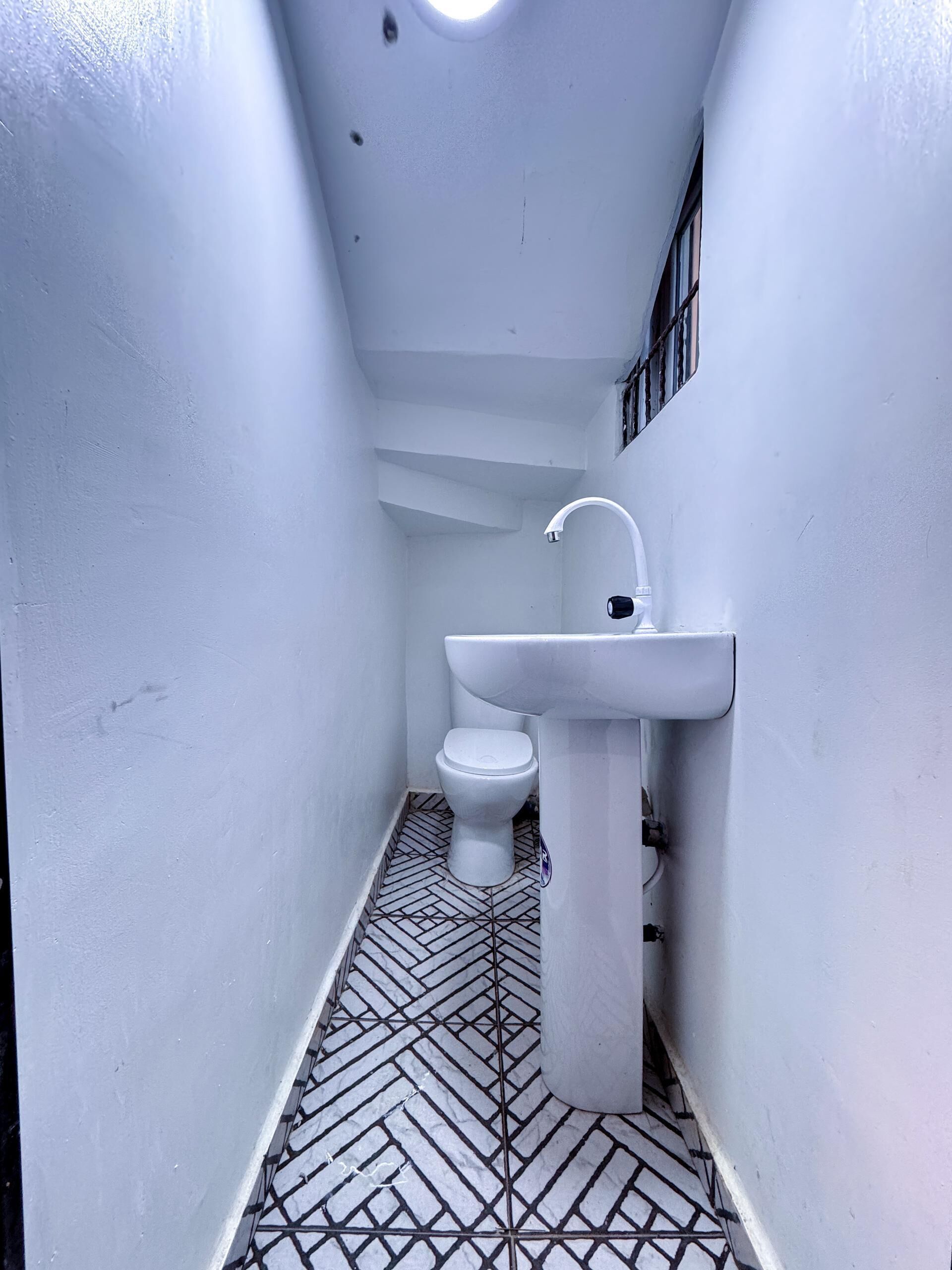 A narrow bathroom with a white toilet, a white sink, and a patterned floor.
