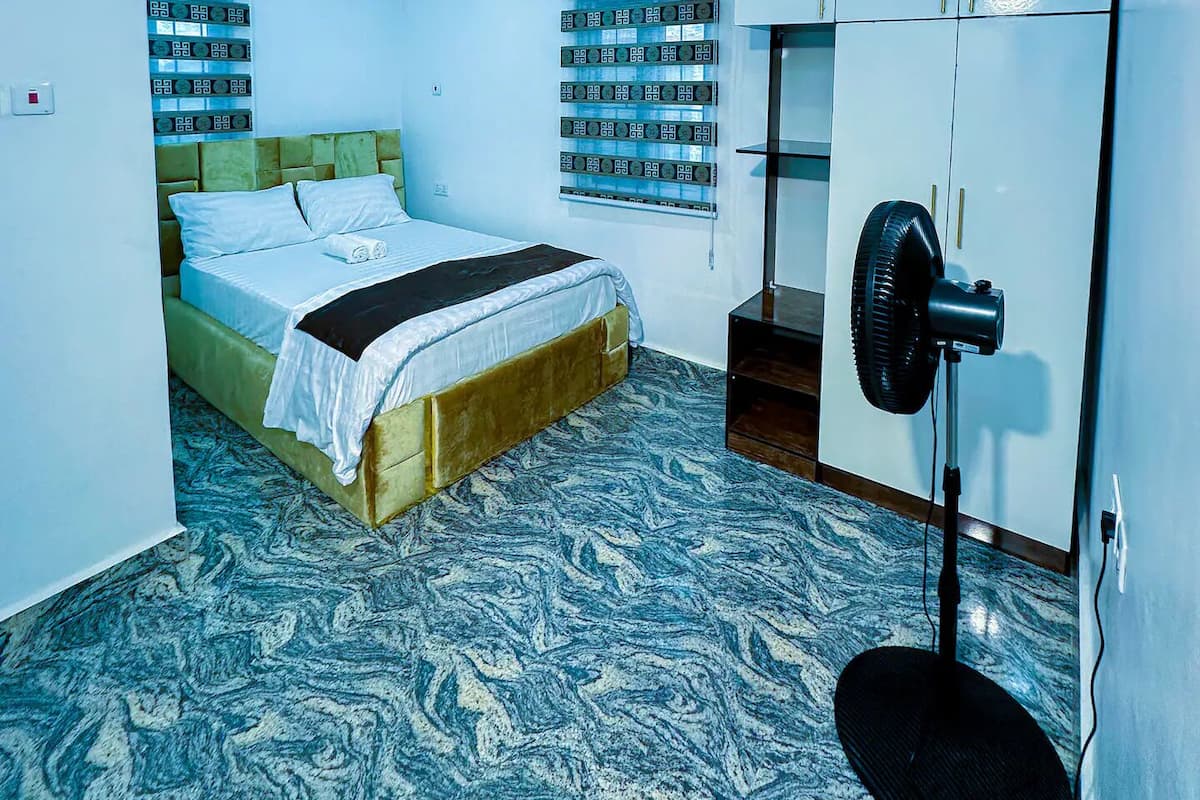 Ein modernes Schlafzimmer mit Bett, Kleiderschrank und Standventilator.