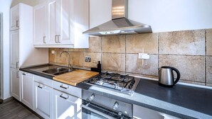 A modern kitchen with white cabinets, a gas stove, a stainless steel range hood, and a tiled backsplash. - Duomo collection suites B (Florencia)